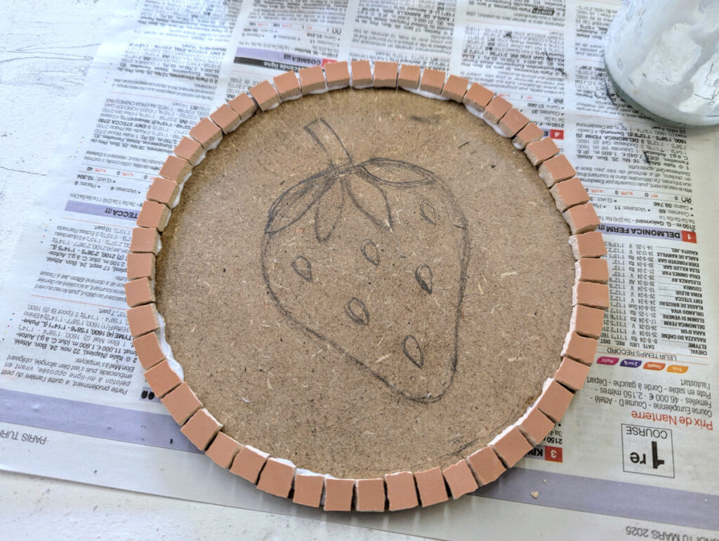 Photo montrant les premières étapes de l'atelier de mosaïque: esquisse au crayon puis collage des carreaux sur la bordure extérieur